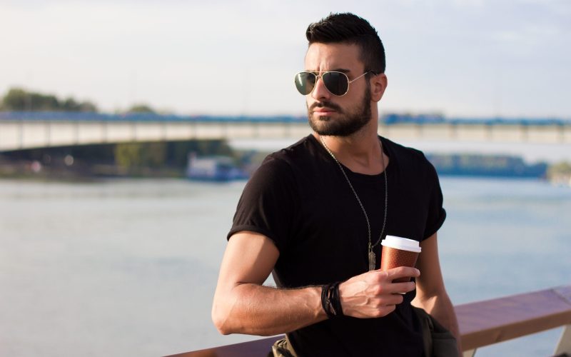 Handsome man outdoors drinking coffee. With sunglasses, a guy with beard. Instagram effect.